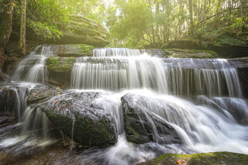 Obraz premium Beautiful large waterfall flowing between rocks in a deep green forest. Waterfall flowing over rocks. Nature background.