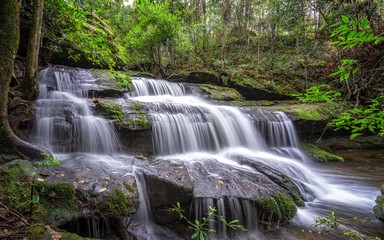 Fototapeta na wymiar Beautiful large waterfall flowing between rocks in a deep green forest. Waterfall flowing over rocks. Nature background.