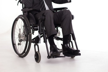 Obraz premium Mans legs in business casual pants in wheelchair. Cropped picture of man wearing formal suit and black shiny shoes sitting in wheelchair.