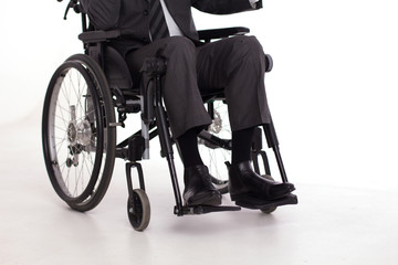 Mans legs in business casual pants in wheelchair. Cropped picture of man wearing formal suit and black shiny shoes sitting in wheelchair.