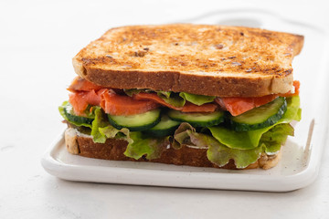 Sandwich with salmon, fresh salad and cucumber on a white board. Copy space.