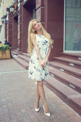 Beautiful blond hair girl in love wearing dress and high heeled-shoes looking away on city street.