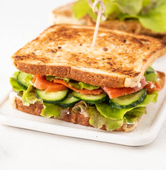 Sandwich with salmon, fresh salad and cucumber on a white board. Copy space.