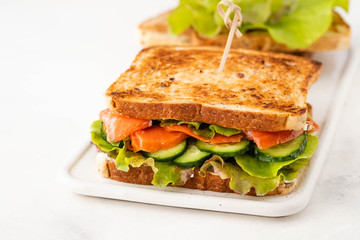 Sandwich with salmon, fresh salad and cucumber on a white board. Copy space.