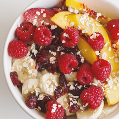 Healthy breakfast with oats, raspberry, nectarine, banana, plum and dried cranberry. Top view, square photo