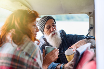 Old hipster couple sitting in a van and looking at a road map  - Powered by Adobe