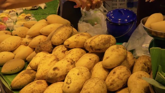 Green grocer sales mango to customer, pass by hand and weigh it
