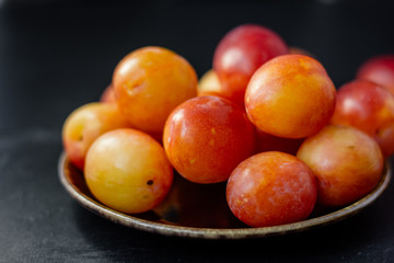 Wild and ripe wild plums on rustic ceramic plate over black background.