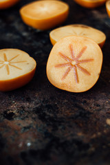 Halves of persimmon fruit on black metal surface.
