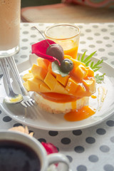 Mango Mousse Cheesecake with fresh mango and sweet mango castade topping and rosemary sprig and cherry on top, on white plate