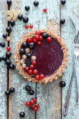Raw vegan pie with berry jam and organic currants on blue background