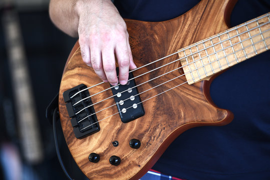 A closeup of a man playing a 5 string bass guitar.