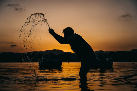 .Young man with funny and relaxed attitude, playing at the seashore throwing water towards the sky at sunset. Lifestyle.