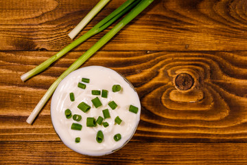 Glass bowl with sour cream and green onion on wooden table. Top view