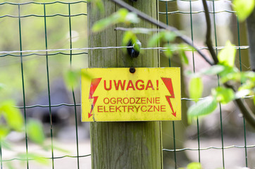Warning sign with a live fence in polish language (uwaga ogrodzenie elektryczne pod napieciem). - obrazy, fototapety, plakaty