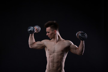 Fototapeta na wymiar Muscular bodybuilder guy doing exercises with dumbbells over black background