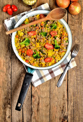 View from above of tuna risotto with vegetables, tomatoes, broccoli and parsley in the old pan, onions, cans and oil in the background - vertical photo