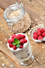 Yogurt with oatmeal and fresh raspberries in a glass and mint leaves, full glass of oatmeals in background - vertical photo