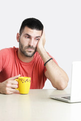 Portrait of young tired handsome young man drinking coffee in front of laptop