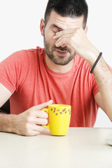 Studio portrait of young handsome man with cup of coffee rubbing his eyes, waking up, feeling tired or bored concept