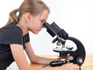 Ein 9 jähriges Mädchen schaut in ein Okular eines Mikroskops. Isoliert vor weißem Hintergrund