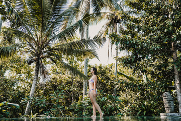 .Young and pretty woman enjoying her vacation in Ubud, in the Bali island, Indonesia. A summer afternoon in the pool with a tropical background. Relaxed and happy attitude. Lifestyle.