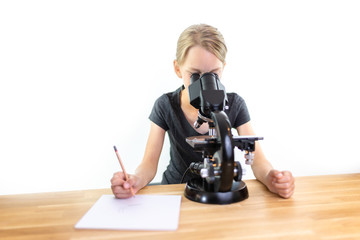 Fototapeta na wymiar Ein 9 jähriges Mädchen schaut in ein Okular eines Mikroskops und notiert ihre Beobachtungen auf ein Blatt Papier. Isoliert vor weißem Hintergrund