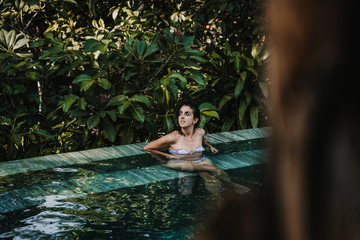 .Young and pretty woman enjoying her vacation in Ubud, in the Bali island, Indonesia. A summer afternoon in the pool with a tropical background. Relaxed and happy attitude. Lifestyle.