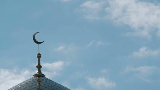 The golden crescent on top of the Islamic mosque close-up. Birds and clouds in the blue sky above the minaret.