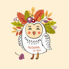 a cute owl with a wreath of autumn leaves and berries on his head with the inscription autumn is here and the leaf
