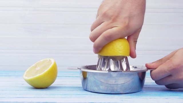 Hands Squeezing Fresh Organic Bio Lemons With Shiny Stainless Steel Juicer On Blue And White Blue Board Closeup