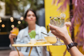 Refreshing cocktail. Elegant woman wearing black leather wrist watch holding glass with refreshing cocktail