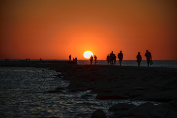 people enjoying sunset on the brakewater in the sea