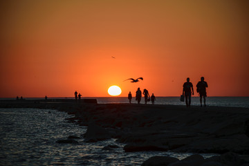 people enjoying sunset on the brakewater in the sea
