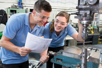 Engineer Instructing Female Apprentice On Use Of Drill