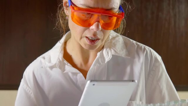 chemist woman is wearing protective glass is reading from display of a tablet in a laboratory