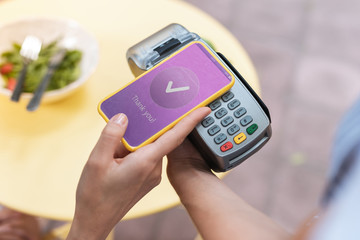 Pay pass. Modern woman paying for her salad while holding her smart phone in hand