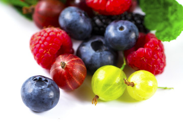 Close-up arrangement mixed, assorted berries including blackberries, strawberry, blueberry, raspberries and fresh leaf on white