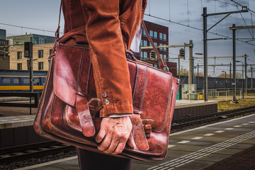 Business passenger in corduroy jacket with leather briefcase close-up, waiting train on station.