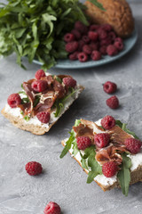 Sandwiches with whole grain bread, homemade cheese, arugula, ham and juicy raspberry. Healthy snack.