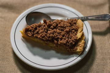 white plate with an apple pie slice  on a wooden background, a vintage spoon and a brown cloth 