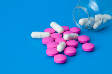 Large and bright red and white pills are scattered from a glass jar. On a blue background.