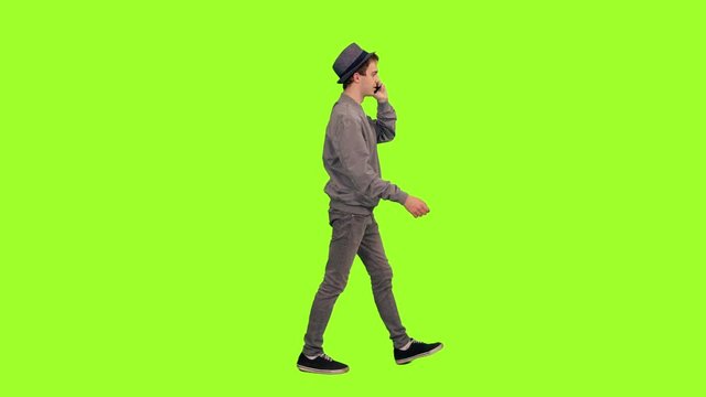 Young hipster man talking on phone while walking on green chroma key background