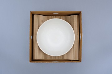 White plate in a box on a gray background. Concept of storage, feeling safe, protect, relocation
