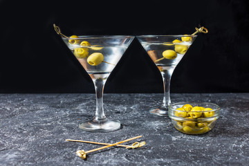 Martini cocktail with green olives on stone table background.