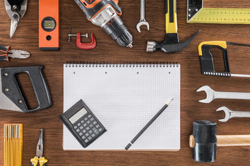 top view of empty textbook, calculator and pencil surrounded by arranged various tools on wooden table
