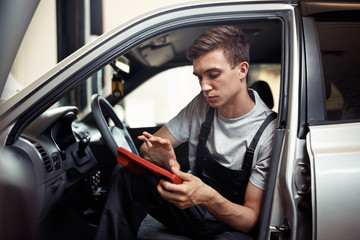 Checking a car at autoservice: a young mechanic is looking for bugs
