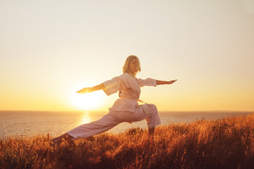Karate girl in a white kimono on the beach, silhouette during training, meditation. Japanese traditional martial art. The concept of a healthy lifestyle.
