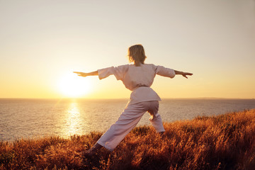 Karate girl in a white kimono on the beach, silhouette during training, meditation. Japanese traditional martial art. The concept of a healthy lifestyle.
