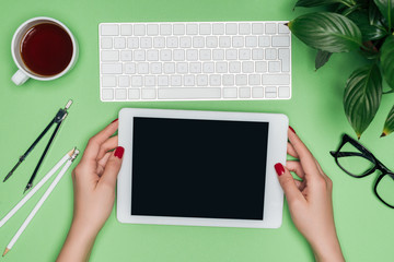 cropped image of female architect holding digital tablet with blank screen at table with divider, coffee and potted plant